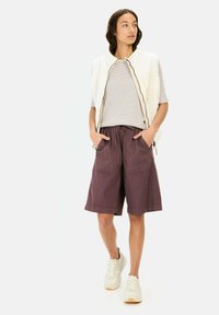 Informele outfit bestaande uit een crèmekleurige vest, gestreepte korte mouwen shirt, kastanjebruine shorts met zakken en lichtgekleurde sneakers.