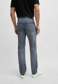 Jeans dritti di un grigio chiaro con un leggero motivo di scoloritura. Presentano tasche posteriori tradizionali e un'etichetta del marchio nera in vita.