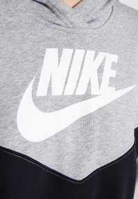 Gray hoodie with black accents, featuring a large white Nike logo. Made of soft fabric with a textured finish and prominent stitching details.