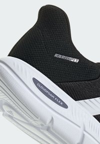 Chaussure de sport noire avec une tige en mesh, une semelle extérieure blanche et l'étiquette "CLOUDFOAM FLEX". Élément clé du design : une coupe sans couture semblable à une chaussette.