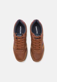 Hnědé kožené tenisky s texturovaným povrchem, kulatou špičkou a kontrastními tmavě modrými a červenými akcenty po stranách a na jazyku. Šněrovací design.