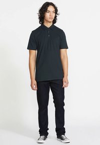 Czarna koszulka polo z bawełny, z kołnierzykiem i trzema guzikami, zestawiona z ciemnymi dżinsami i trampkami.