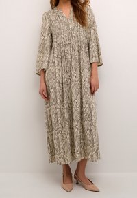 Femme portant une robe midi à manches longues marbrée beige et marron avec un corsage froncé et des chaussures à talons kitten beige à l'arrière.