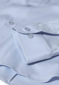 Svijetloplava košulja s glatkom teksturom tkanine, koja ima upućeni ovratnik i gumbe na manžetama. Klasičan kroj s preciznim šavovima.