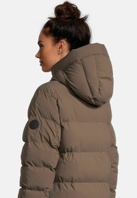 Braune Pufferjacke mit Kapuze, ausgestattet mit gesteppten Bereichen, einem schwarzen Logo-Patch am Ärmel und einer glatten, strukturierten Oberfläche.