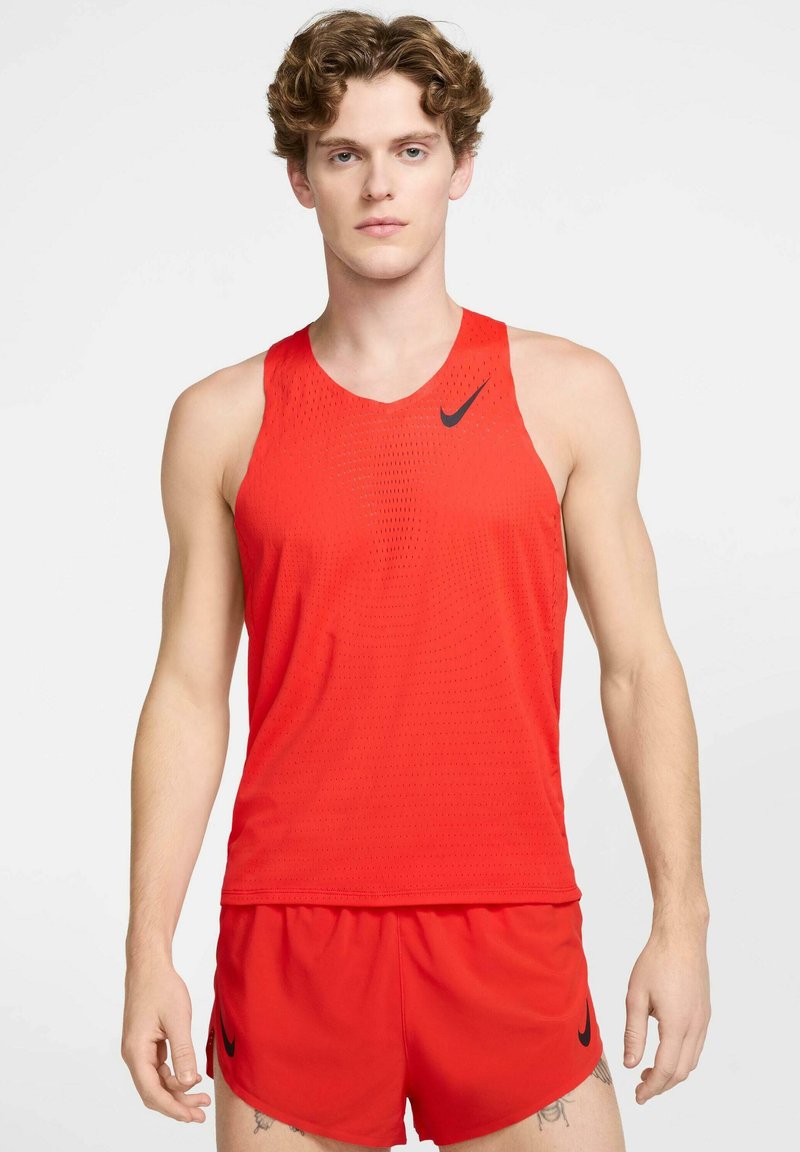 Punane sporditop võrgutaolisest kangast, millel on must Nike logo. Koos sobivate punaste lühikestega. Lihtne lõige ja hingav disain.