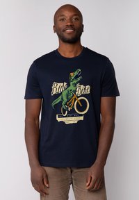 Marineblauwe t-shirt van katoen, met een grafische print van een dinosaurus die op een fiets rijdt, met tekst eronder, wat een leuk thema illustreert.