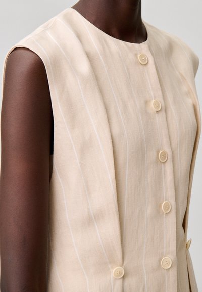 Top sin mangas beige con rayas blancas verticales, cuello redondeado y cuatro botones claros al frente.