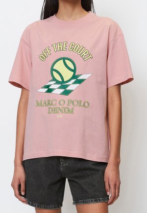 Persoon draagt een roze T-shirt met tennisbal en geruit veld grafiek, tekst "OFF THE COURT", zwarte denim shorts.