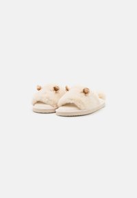 Faux fur slippers in cream with a wide band and small, rounded accents. Soft texture and flat, rubber sole for comfort.