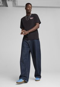Sort bomulds t-shirt med grafisk design, parret med løstsiddende mørk denim jeans og blå sneakers med gummisål.