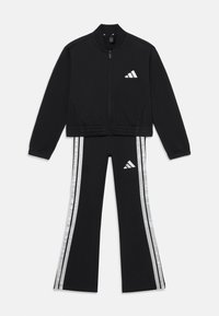 Chándal negro que incluye una chaqueta con cremallera y pantalones acampanados. Rayas plateadas a los lados y un pequeño logo en la chaqueta y la cinturilla.