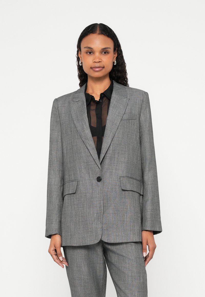 Szara marynarka w kratę z klapą z wycięciem, pojedynczym czarnym guzikiem i dwoma przednimi kieszeniami. W połączeniu z przezroczystą czarną bluzką. Gładka faktura tkaniny.