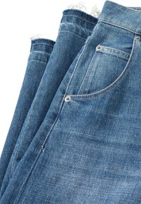 Jeans en denim dans une teinte bleue moyenne avec des ourlets effilochés, featuring des poches standard et du matériel argenté sur la poche avant. Texture lisse.
