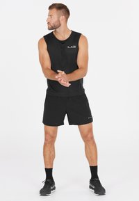 Musta ilmanhiha athletic-paita ja siihen sopivat shortsit, jotka on valmistettu kevyestä kankaasta. Varustettu logoesittelyillä ja rentolla istuvuudella. Mustat urheilukengät.