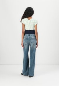 Striped, light green short-sleeve top with a scalloped neckline, paired with blue wide-leg jeans and black footwear, viewed from the back.