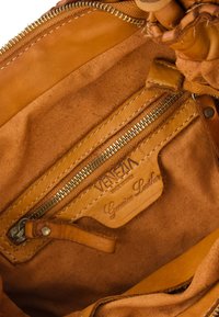 Brown leather handbag interior featuring a zippered pocket, labeled "VENEZIA," with a soft fabric texture and reinforced stitching details.