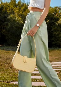 Borsa gialla con texture a coccodrillo, dalla silhouette curvata e con una tracolla semplice. Pantaloni plissettati verde chiaro e una maglietta bianca.