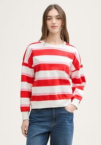 Crveno-bijeli prugasti pulover s ružičastim akcentima, okrugli izrez, dugi rukavi, opušteni kroj, uparen s plavim trapericama. Mekana tekstura materijala.