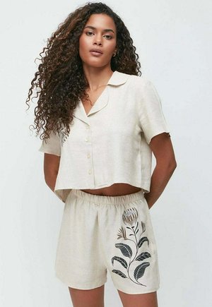Leinen-Zweiteiler bestehend aus einem kurz geschnittenen, knopfbaren Oberteil in hellbeige und Shorts mit elastischem Bund, verziert mit floraler Stickerei in dunklen Farben.
