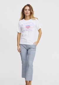 Balta marškinėliai su spalvingu grafiniu piešiniu, kuriame užrašyta "California" ir "World Tour." Derinami su šviesiai pilkais languotais keliais, tiesaus kirpimo.