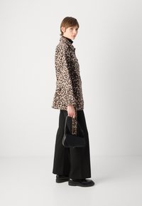 Veste en imprimé léopard avec une coupe décontractée, associée à un pantalon noir à jambe large et un petit sac à main noir. Textures lisses et motifs audacieux.