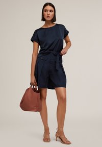 Top scurt din satin bleumarin cu mânecă scurtă, asortat cu pantaloni scurți bleumarin cu curea, având buzunare laterale. Accesorizat cu o geantă texturată în nuanța arămie și sandale cu curea nude.