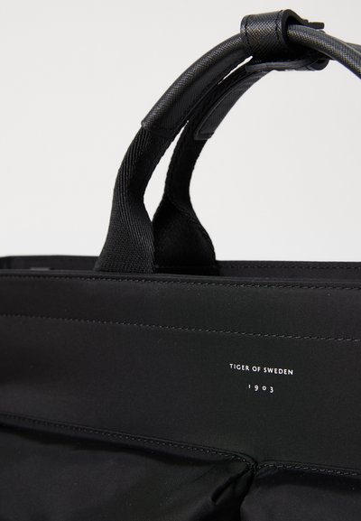 Sort nylon håndtaske med dobbelt teksturerede håndtag. Har præget logo, rene linjer og et enkelt design. Fokuserer på funktionalitet.