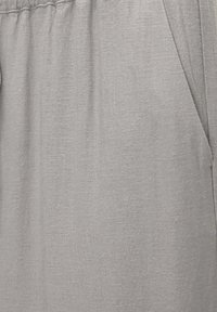 Grijze stof met een gestructureerd oppervlak, voorzien van een gathering met elastische tailleband en zijzakken. Eenvoudig, functioneel ontwerp.