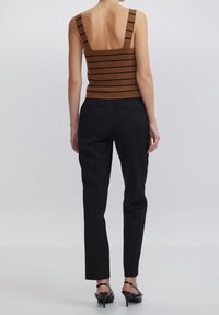 Tirantes anchos de camiseta sin mangas a rayas marrones, combinada con pantalones negros ajustados. El conjunto presenta una silueta entallada y un detallado mínimo.