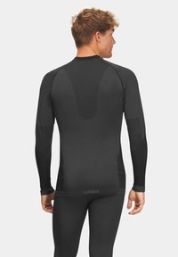 Czarna, długozasłonowa warstwa bazowa o dopasowanym kroju, z panelami siateczkowymi dla lepszej wentylacji oraz płaskimi szwami dla komfortu. Logo marki na dolnym brzegu.
