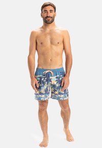 Blaue Badehose mit einem Muster aus Palmen und Sonnenuntergang, ausgestattet mit einem elastischen Bund und Kordelzug. Das Material hat eine glatte Textur.