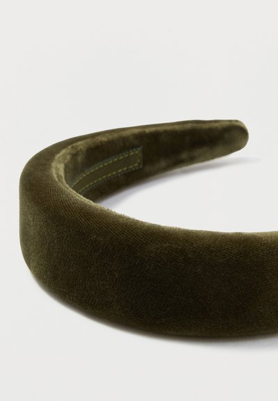 Diadema de terciopelo en verde oliva oscuro. Textura suave con un diseño ancho y redondeado, y un detalle de costura amarilla en contraste en el lado interior.