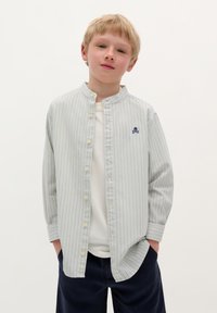 Camicia a righe con bottoni, caratterizzata da colori blu chiaro e bianco, colletto alla mandarino e un piccolo logo a forma di teschio navy sul petto.