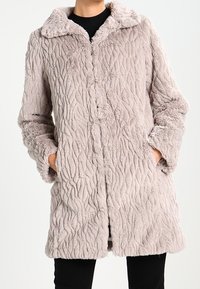 Ljusbrun, texturerad fuskpälsjacka med krage, långa ärmar och sidofickor. Har ett vågigt mönster och knappstängning.