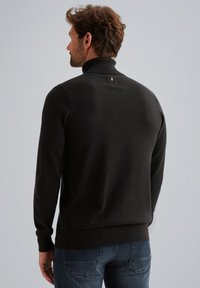 Maglione nero a maglia con colletto alto e orlo a coste. Presenta un piccolo logo metallico sul retro, maniche aderenti e una texture liscia.