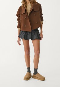 Brązowa krótka kurtka dwurzędowa z dużymi guzikami, zestawiona z ciemną falbaniastego spódnicą i jasnobrązowymi butami wsuwanymi. Miękka tekstura, luźny krój.