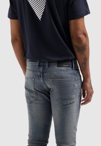 Lichtblauwe, slim-fit jeans met een vervaagde afwerking, voorzien van twee achterzakken en een zwart taillebandlabel met de tekst "PURE PATH."