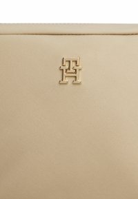 Clutch in tessuto beige con superficie texturizzata, caratterizzato da un accento in metallo dorato nel angolo inferiore.