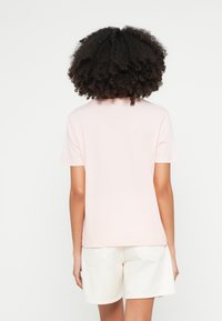 Camiseta rosa claro de manga corta y cuello redondo. Textura suave, ajuste relajado, combinada con pantalones cortos blancos que cuentan con bolsillos traseros.