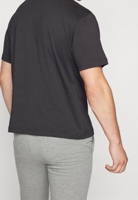 Černé bavlněné tričko s krátkými rukávy, volný střih a prošívané lemy, v kombinaci s šedými slim-fit tepláky. Hladký povrch, minimalistický design.