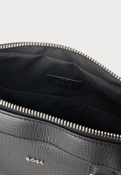 Sac en cuir noir BOSS ouvert, laissant voir sa doublure en tissu noir, sa poche intérieure et sa fermeture éclair argentée.