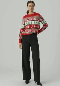 Röd stickad tröja med festliga mönster, inklusive snögubbar och pepparkakor, ihop med svarta byxor med vida ben. Slät textur.