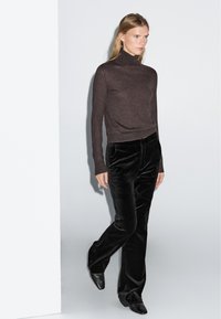 Brun polotröja, figursydd, kombinerad med svarta manchesterbyxor med utsvängda ben. Modellen bär svarta högklackade skor, mot en enkel ljus bakgrund.