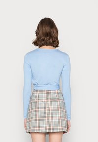 Himmelblaues Langarmoberteil mit tailliertem Design und einer Schleifendetail an der Taille, kombiniert mit einem karierten Minirock in Pastellfarben.