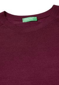 Burgundská pletená svetr s kulatým výstřihem a žebrovanou strukturou. Štítek uvádí "United Colors of Benetton", vyšitý zeleně na vnitřním límci.