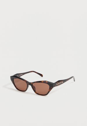 Lunettes de soleil œil de chat en écaille avec verres marron foncé et détails de marque sur les branches, sur fond blanc.