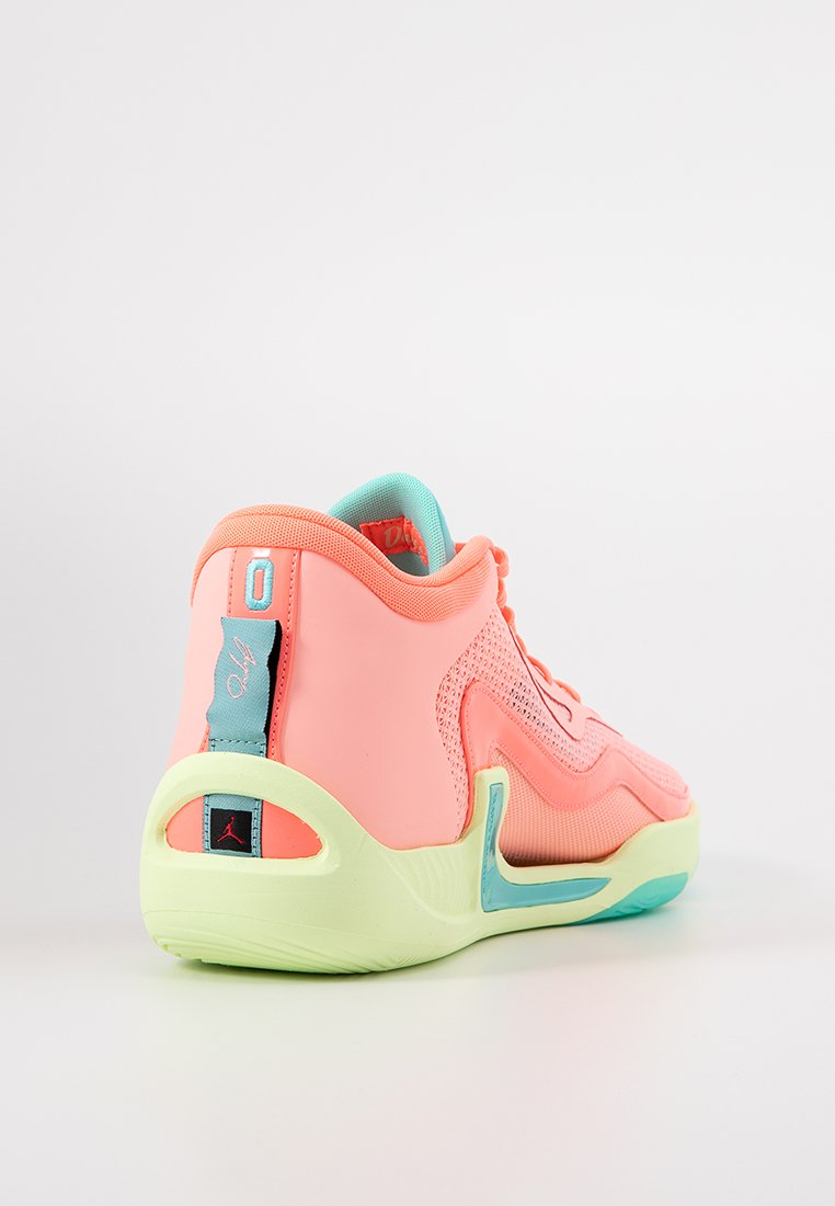 Zapatilla de baloncesto rosa con parte superior de malla y sintético, suela gruesa verde y acentos azules en el talón y la lengüeta.