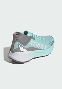 Turkusowy but sportowy z oddychającą cholewką, szarymi akcentami, teksturowaną powierzchnią, wyraźnym logo "TERREX" oraz wytrzymałą białą podeszwą.