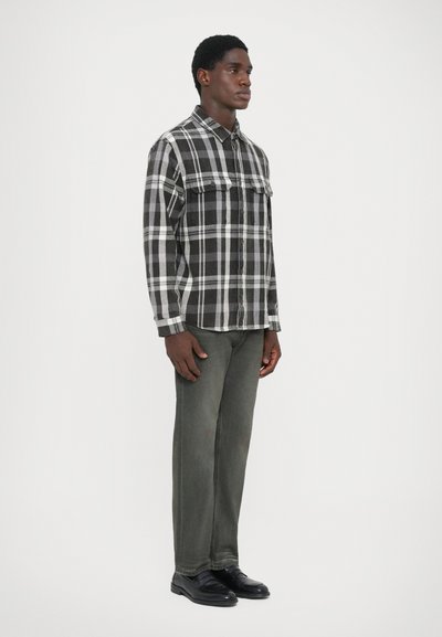 Svart og grå rutete flanellskjorte med to brystlommer, knappelukking, kombinert med grå jeans og svarte sko.